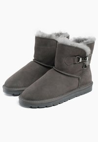 Botines tobilleros de ante gris con un suave forro de piel gris, que presentan una correa lateral y herrajes decorativos. Suela de goma plana para mayor tracción.