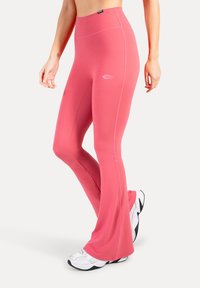 Roze uitlopende legging gemaakt van rekbare stof, met een hoge tailleband en subtiel logodetail, gecombineerd met witte sneakers.