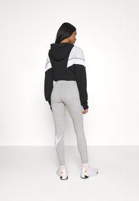 Fekete és szürke kapucnis pulóver világosszürke, fehér Nike logóval díszített leggingssel; a modell fehér sportcipőt visel.