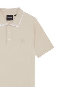 Polo beige realizzato in tessuto liscia con collo a camicia. Presenta tre bottoni e un sottile logo ricamato sul petto. Dettagli con bordo bianco.