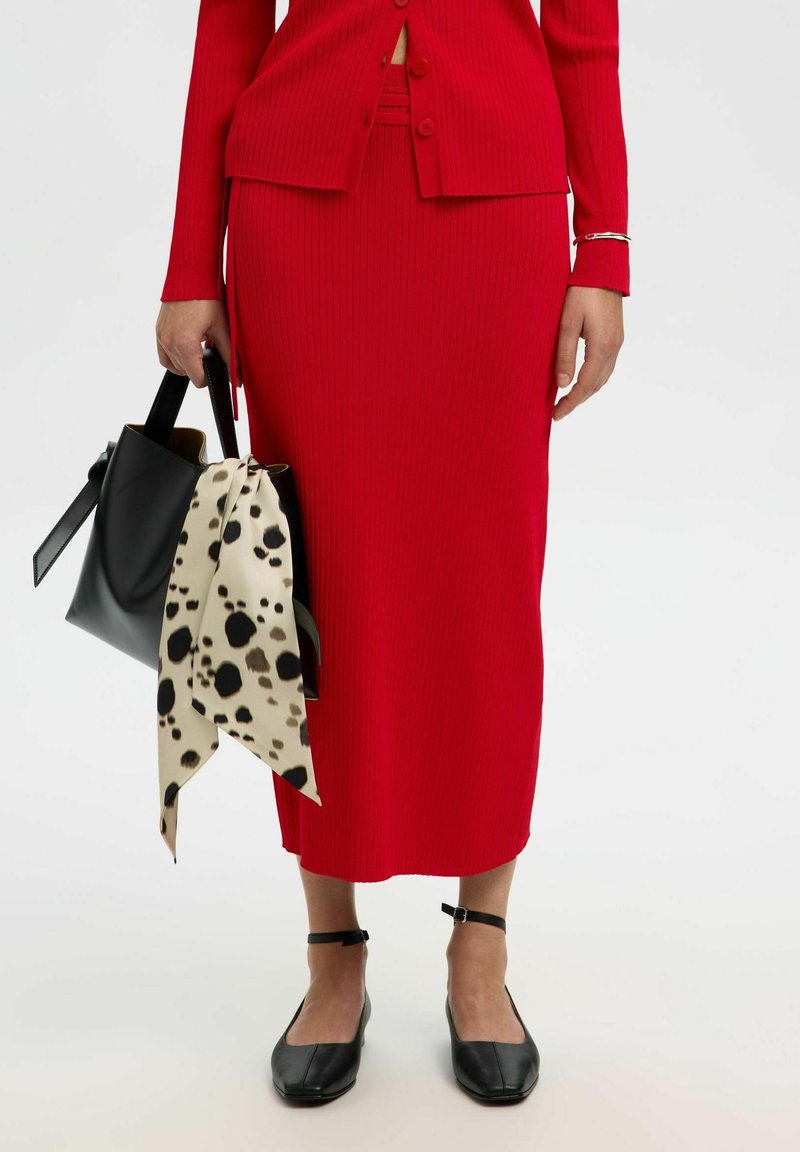 Robe en tricot côtelé rouge avec un cardigan court assorti, accompagnée d'un sac à main noir orné d'une écharpe beige à pois. Ballet flats noirs à bout carré.