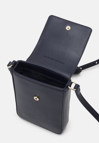 Bolso cruzado de cuero azul marino con forma rectangular plana, herrajes dorados, cierre magnético y logo en relieve en el interior.