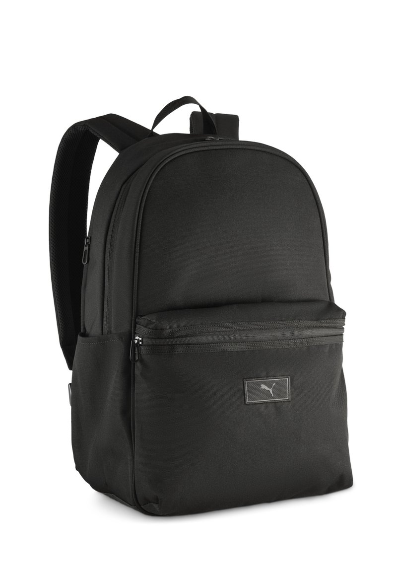 Mochila negra hecha de tela duradera, con forma redondeada, dos compartimentos con cremallera y un discreto parche de logo en la parte frontal.