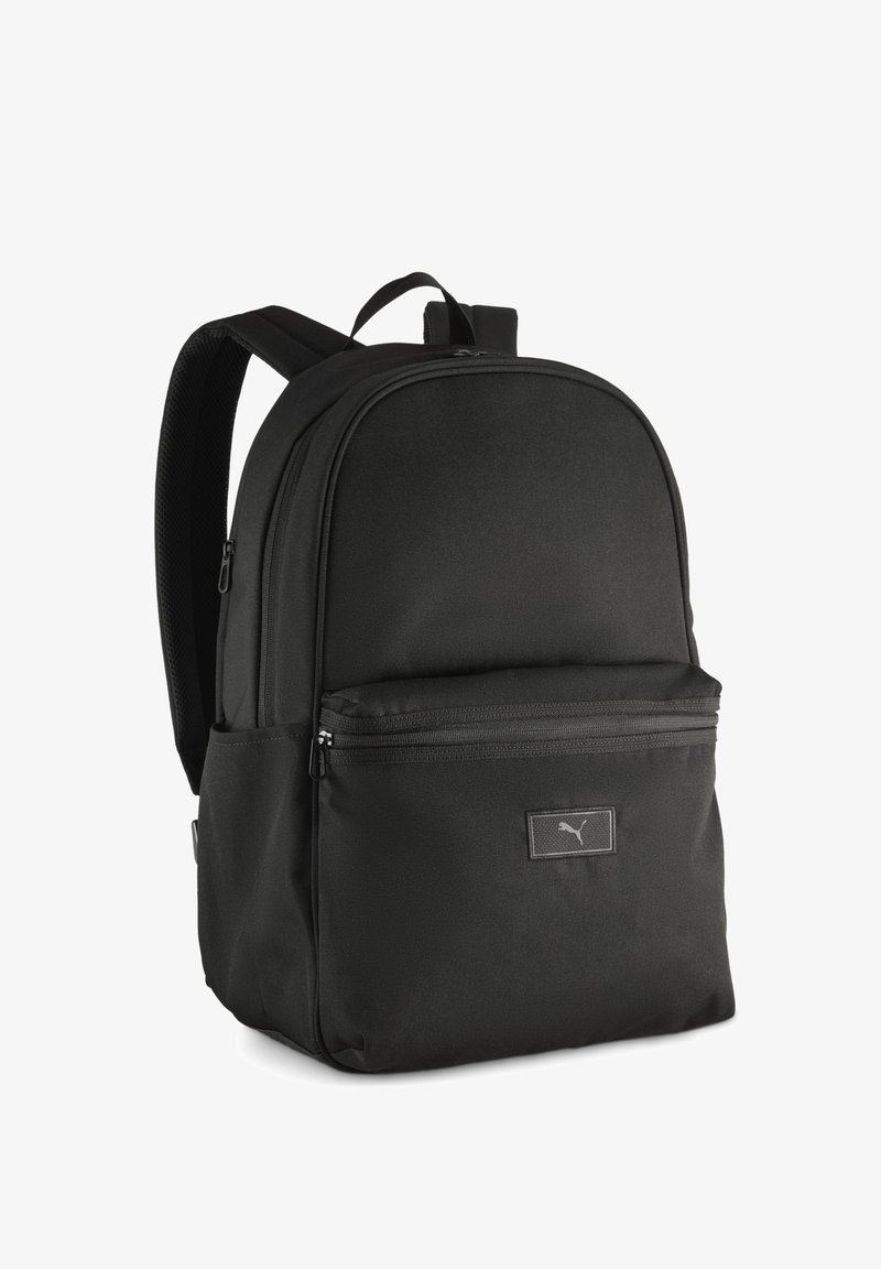 Mochila negra hecha de tela duradera, con forma redondeada, dos compartimentos con cremallera y un discreto parche de logo en la parte frontal.