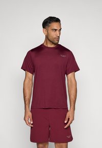 Burgundská športová tričko s krátkymi rukávmi, okrúhlym výstrihom a vystúpeným logom; skombinované s ladnými šortkami, obe z ľahkej tkaniny.