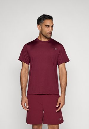 Burgundių spalvos sportinė marškinė su trumpomis rankovėmis, apvaliu kaklu ir reljefiniu logotipu; derinama su atitinkančiomis šortais, abu iš lengvo audinio.