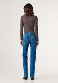 Sinised teksapüksid kitsas lõikega, millel on keskmise kõrgusega vöökoht, tagataskud õmbluse detailiga ja pruuni nahast märk vöörihmadel.