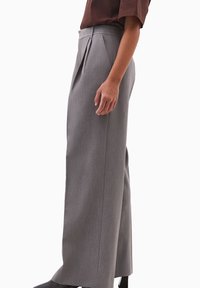 Szare plisowane spodnie cechują się dopasowanym krojem, szeroką nogawką, fakturowaną tkaniną oraz gładkim paskiem w talii z kieszeniami w szwach bocznych.