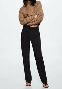 Un pull court en tricot marron à tresses associé à un pantalon noir taille haute. Les pantalons ont une coupe droite et un design minimal.
