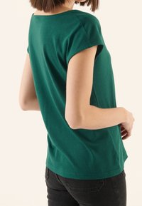 T-shirt a maniche corte verde teal realizzato in cotone morbido, caratterizzato da un collo rotondo e una vestibilità comoda, abbinato a jeans scuri.