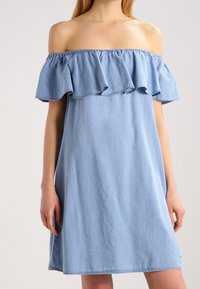 Sinine denim kleit õlgadelt avatud disainiga, rippuva kaeluse ja laia lõikega. Lühike, sirge serv, millel on õrn tekstuur. Nähtavaid kinnitusi ei ole.