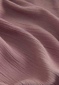 Tissu texturé en mauve atténué, présentant des plis doux et ondulés ainsi qu'un tissage fin qui met en valeur de subtiles variations de couleur et de texture.