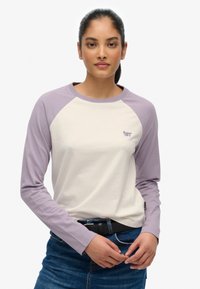 Camiseta de manga larga con cuerpo en crema y mangas raglán en púrpura claro. Presenta un logo bordado en el pecho y está hecha de suave algodón.