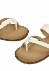 Paire de sandales plates avec semelles beiges et brides en cuir blanc, comprenant un entre-doigts et une bride de cheville.