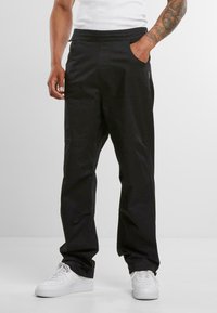 Black pants made of soft fabric, featuring a relaxed fit, elastic waistband, side pockets, and subtle stitching details. Paired with white sneakers.