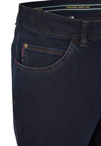 Ciemnoniebieskie dżinsy z pomarańczowym i czerwonym przeszyciem, kieszenią z przodu oraz metalowym guzikiem. Tkanina ma gładką teksturę i dobrze dopasowany krój.