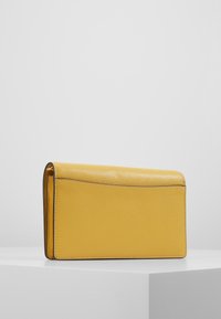 Portefeuille en cuir jaune avec une finition texturée, de forme rectangulaire et des bords cousus, présentant un accent embossé subtil le long du dessus.