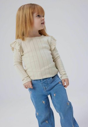 Cream long-sleeve top with ruffled shoulders, textured stripes. Light blue jeans with colorful ice cream cone embroidery.