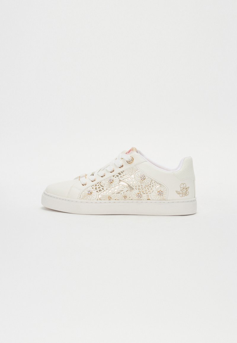 Sneaker bianco con motivo a fiori ritagliato e dettagli dorati. Presenta lacci rotondi, suola testurizzata e un tab posteriore verde chiaro.