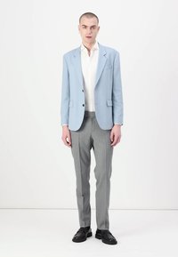 Blazer azul claro de tela lisa, combinado con una camisa blanca y pantalones grises. Los zapatos son negros con una suela gruesa.