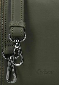 Detail van een groene leren handtas met een zilveren metalen rits met twee clips en contrasterende stiksels. Gegraveerd 'Gabor' logo zichtbaar.