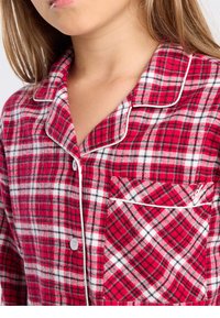 Rood-wit geruit flanellen pyjamabloesje met een kraag, witte bies en een borstzak met een diagonaal ruitpatroon. Drukknoopsluiting.