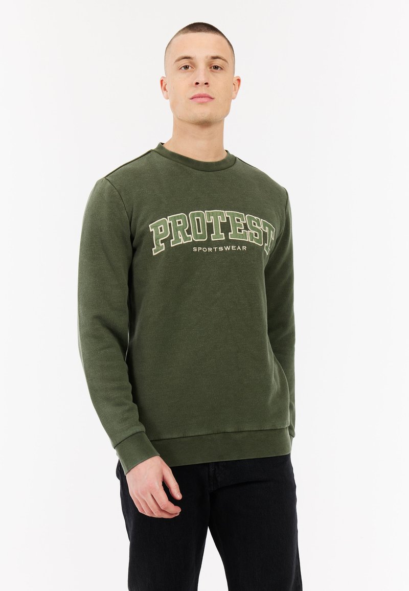 Groene sweatshirts met ronde hals en "PROTEST" en "SPORTSWEAR" gedrukt in vetgedrukte witte en groene letters; heeft lange mouwen en ribgebreide manchetten.
