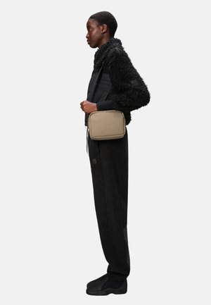 Chaqueta texturizada negra, bolso rectangular beige, pantalones y zapatos negros; líneas limpias y diseño funcional, visto de perfil.