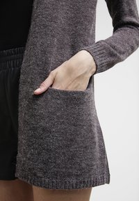 Long, gray cardigan made of soft, textured knit fabric featuring a side pocket and ribbed cuffs, suitable for layering.