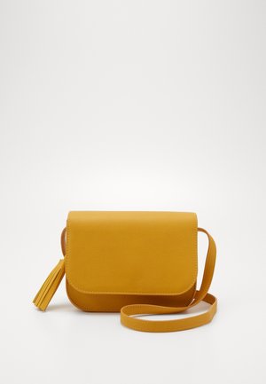 Lille mustardgul crossbody taske med flaplukning, matchende kvastdetalje og justerbar skulderrem på hvid baggrund.