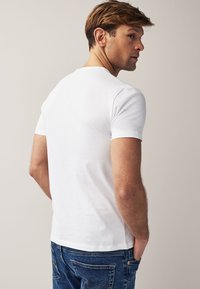 Maglietta bianca in cotone con maniche corte, scollo tondo, trama liscia e vestibilità casual, abbinata a jeans di denim blu.