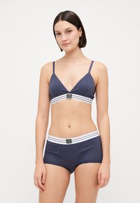 Navyblauwe katoenen bralette met verstelbare banden en een wit gestreepte band; bijpassende navyblauwe hipster shorts met logo tailleband.