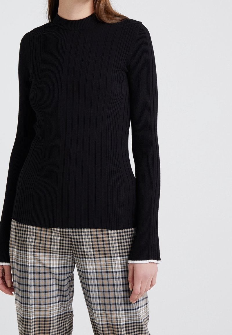 Zwarte geribbelde lange mouw top met een hoge hals, voorzien van een textuurdesign. Gecombineerd met een broek met ruitpatroon in neutrale tinten.