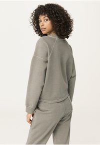 Sudadera de color gris claro, con cuello acanalado y mangas raglán, y cinturilla ajustable. Tejido suave, corte relajado, con detalles de costura mínimos.
