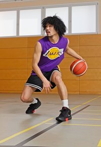 Vijoličasta brezrokavna košarkarska majica z logotipom "Los Angeles Lakers", črne hlače s belimi črtami, črne košarkaške čevlje, dribla žogo.