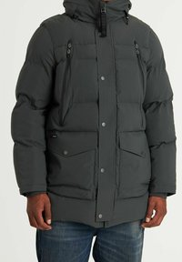 La chaqueta acolchada de color gris oscuro cuenta con un cierre frontal con cremallera, capucha ajustable y múltiples bolsillos con cierres de botón a presión. Textura suave y diseño elegante.