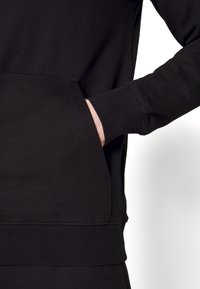 Svart sweatshirt med långa ärmar, ribbade muddar och en framficka. Tillverkad av mjukt material med en slät yta och en avslappnad passform.