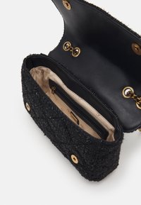 Zwarte handtas met een gestructureerd oppervlak, een pluizige buitenkant, goudkleurige hardware en een satijnen voering met een zakje met rits en een drukknoopsluiting.