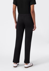 Schwarze Sweatpants mit entspannter Passform, elastischem Bund und glatter Textur, kombiniert mit weißen und braunen Sneakern.