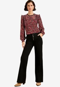 Blusa rossa e nera con motivo a righe, maniche lunghe e rouches, abbinata a pantaloni neri a vita alta con bottoni e tasche.