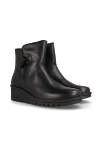 Botas de tobillo de cuero negro con puntera redonda, tacón de cuña de goma y un detalle de botón decorativo en el lado exterior. Textura suave.