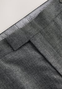 Tessuto grigio con texture, rivestito internamente da una fodera liscia e dotato di un waistband strutturato, presenta una parte frontale piatta e minimi dettagli.