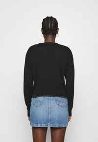 Maglione nero con orlo e polsini a coste, abbinato a una gonna di jeans blu con due tasche posteriori e silhouette dritta.