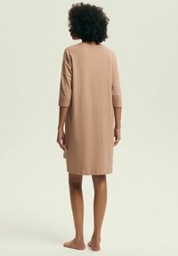 Sukienka do kolan, luźna, w jasnobeżowym kolorze, wykonana z miękkiego materiału, z rękawami o długości trzech czwartych i okrągłym dekoltem.