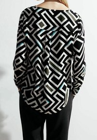 Blusa a righe in bianco e nero con motivi geometrici e accenti turchesi e oliva. Realizzata in tessuto leggero, con una vestibilità ampia.