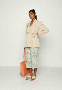 Blusa bege com cinto, culotes verdes florais, mala laranja e sandálias de creme. O conjunto apresenta um tecido suave com detalhes de padrão floral.