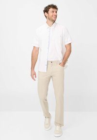 Kortubben wit overhemd, lichtbeige broek en crèmekleurige sneakers. Het overhemd heeft een blauwe gestreepte accent bij de sluiting.