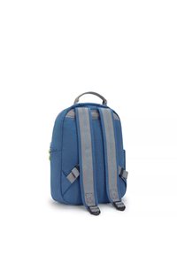 Mochila de tela azul con correas de hombro grises, parte superior redondeada, bolsillo lateral y asa superior. Textura suave, diseño minimalista.