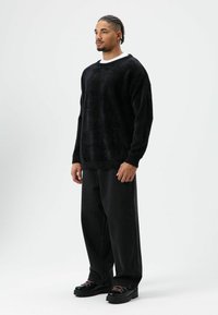 Zwarte, pluizige trui met een losse pasvorm, gecombineerd met wijde zwarte jeans en grove zwarte schoenen met gekleurde veters. Eenvoudig wit ondershirt zichtbaar.