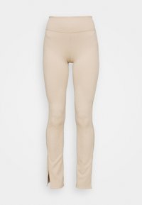 Beige ribbade leggings med hög midja, som har sidoklipp vid anklarna. Tyget verkar elastiskt och texturerat.